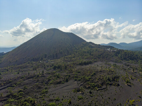 Aerial view of the volcanic cone of Volcan Paricutin surrounded by vast lava fields and sparse vegetation under a blue sky in Uruapan, Michoacan, Mexico.