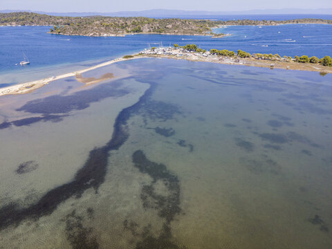 Aerial view of Nisis Dhiaporos island featuring turquoise shallow waters, sandy spits, pine trees, and docked boats in Halkidiki, Greece.