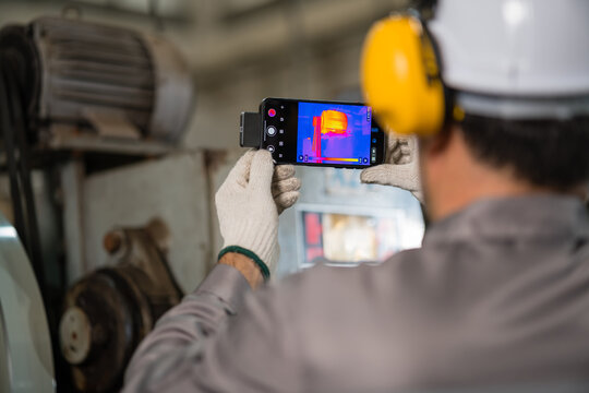 Technician checking motor temperature with a handheld thermal camera showing a heat map and temperature scale on screen