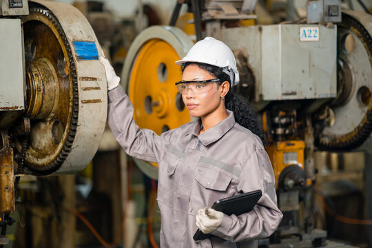 Female engineer in a hard hat holding a digital tablet beside the flywheel of a mechanical power press