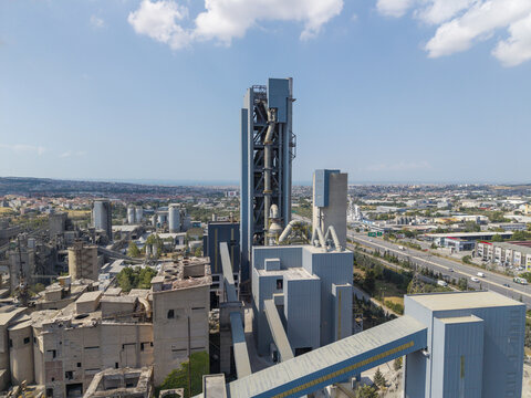 Aerial view of the TITAN Cement factory featuring large industrial silos, conveyor systems, and manufacturing buildings in Thessaloniki, Central Macedonia, Greece.
