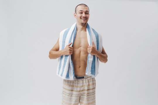 Smiling Shirtless Young Man Holding Beach Towel on Grey Background
