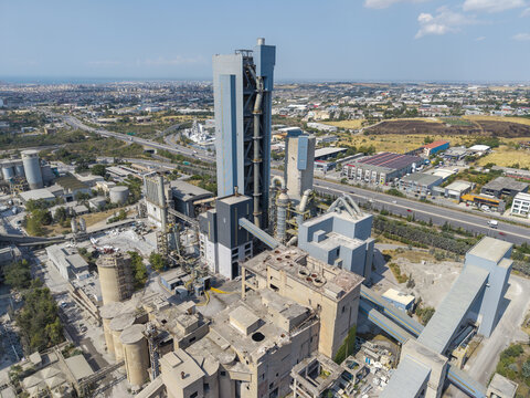 Aerial view of the TITAN Cement factory featuring large industrial silos, complex conveyor systems, and surrounding infrastructure in Thessaloniki, Central Macedonia, Greece.