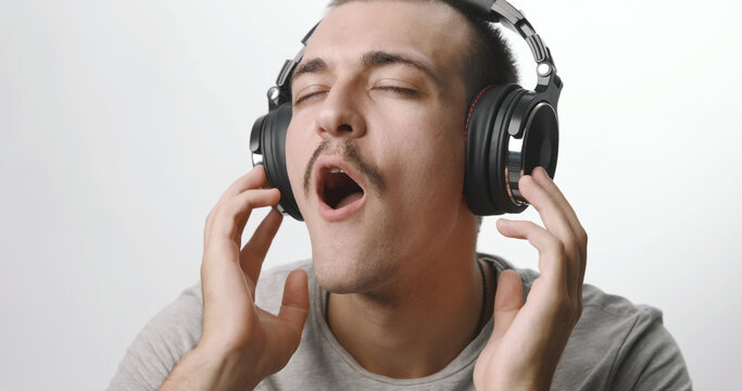 Young man wearing headphones listening to music with eyes closed and mouth open against a white background.
