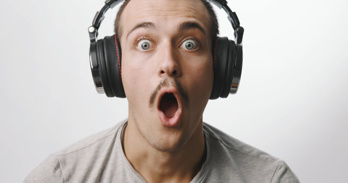 Surprised and shocked young man wearing headphones looking at camera on a white studio background.