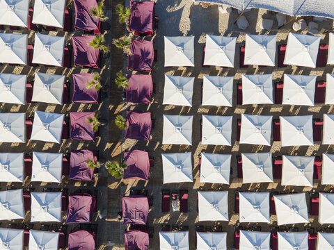 Aerial view of Trani Ammos Beach featuring rows of white and purple beach umbrellas arranged on the sandy shore in Trani Ammouda, Greece.