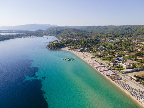 Aerial view of Trani Ammos Beach featuring turquoise waters, rows of sun loungers, and a floating water park along the coastline in Trani Ammouda, Greece.