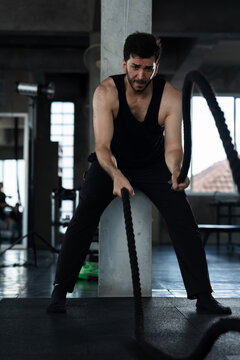 Adult Caucasian man gripping battle rope in modern gym, male athlete pushing arms forward during functional strength training, endurance workout routine, sports motivation, healthy lifestyle content