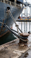 Obraz premium Vertical close-up of thick mooring ropes secured from a container ship to a rusted quay bollard during safe cargo vessel berthing