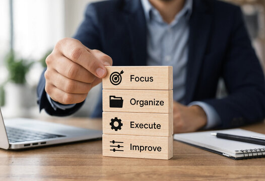 Businessman stacking wooden blocks with words Focus Organize Execute Improve and icons representing each step of a process on a desk with a laptop transparent background