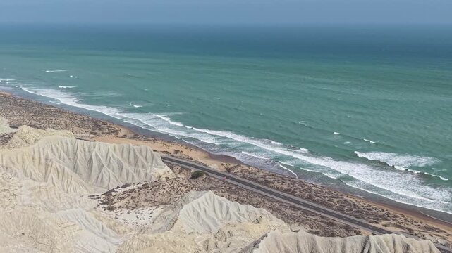 Aerial drone view of the Makran Coastal Highway in Balochistan, Pakistan, winding through rugged mountains along the Arabian Sea, showcasing dramatic coastline, scenic landscapes, and stunning natural