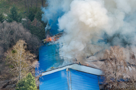 Aerial view of firefighters extinguishing a large building fire with heavy smoke billowing from the blue roof in Belgrade, Serbia.