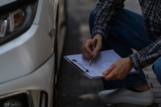 Asian car insurance agent inspecting damage on headlight of white car.