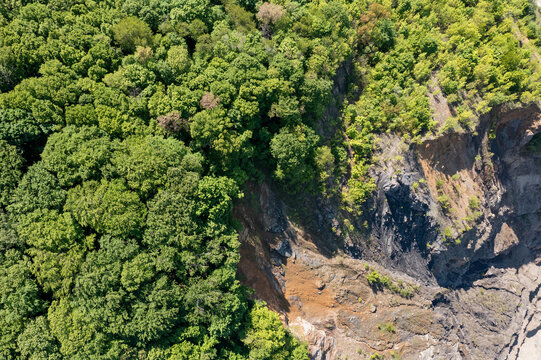 Aerial view of a quarry with steep rocky cliffs, a small pond at the bottom, and a winding road bordered by lush green trees in Rakovac, Vojvodina, Serbia.