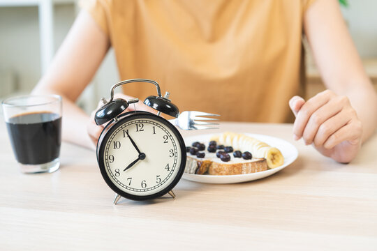 Closeup of alarm clock showing eight AM with fork pointing to healthy breakfast fruit toast, intermittent fasting weight loss concept, time restricted eating nutrition plan and diet lifestyle.