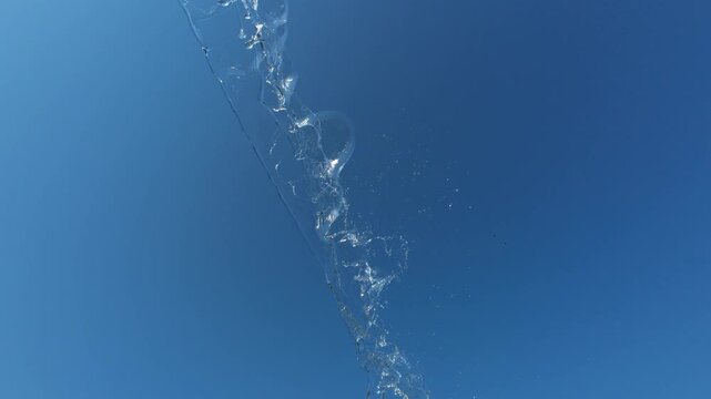 Dynamic Water Stream Splashing Diagonally Across Blue Sky with Birds Flying