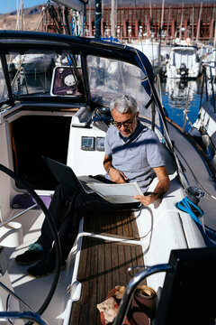 Focused senior captain reading document at helm of sailboat