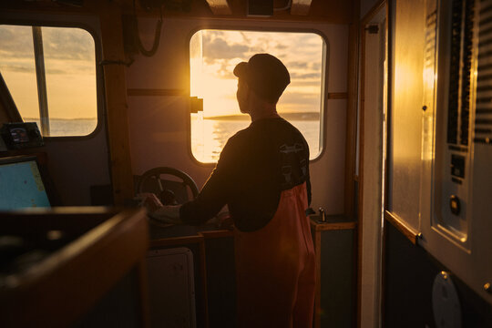 A female boat captain navigates waters at sunset near the coast