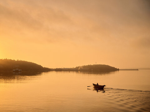 Rowing a small dory boat on calm water during sunset near the shore