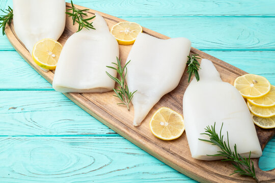 Fresh raw squid tubes with lemon slices and rosemary on wooden board