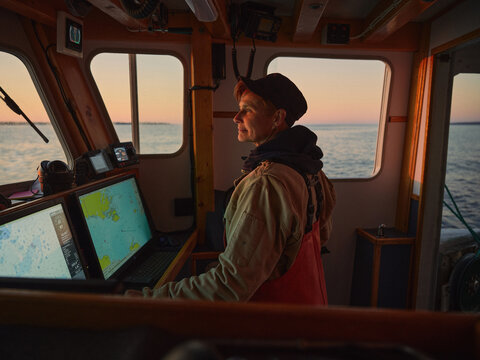 A female boat captain navigates waters at sunset near the coast