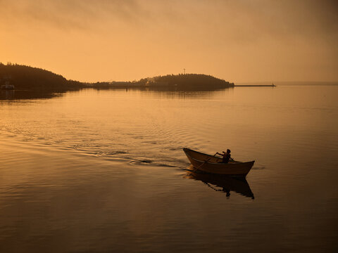 Rowing a small dory boat on calm water during sunset near the shore