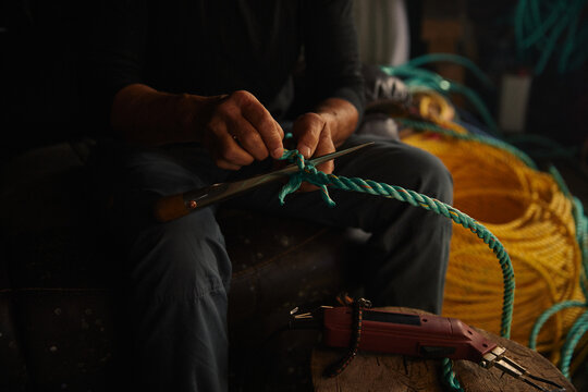 A fishing boat captain mending ropes in her old workshop
