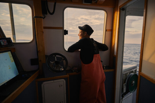 A female boat captain navigates waters at sunset near the coast