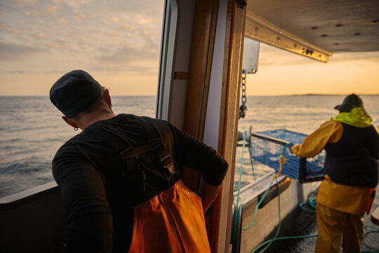 Fishermen prep lobster traps on a boat at sunset in open water