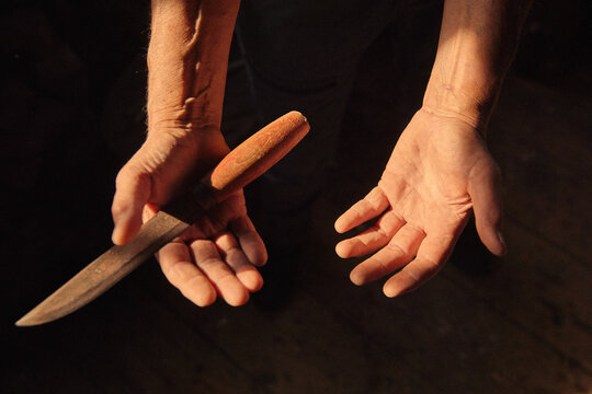 Hardened hands hold a knife ready for a task in a dim light setting