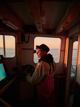 A female boat captain navigates waters at sunset near the coast
