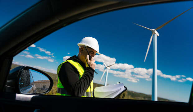 Engineer communicating near wind turbine at renewable energy farm