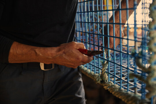 Lobster fisherman fixes rope on lobster trap in a workshop by the sea