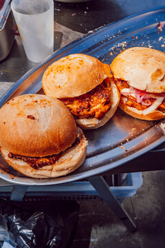 Three fresh burgers on a metal tray at a street food market