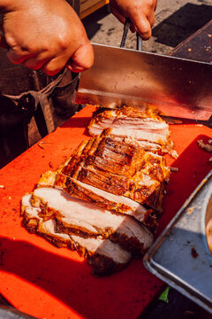 Chef carving a large piece of crispy roasted pork belly