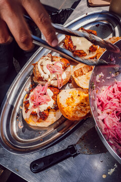 Chef using tongs to assemble pork burgers with pickled onions