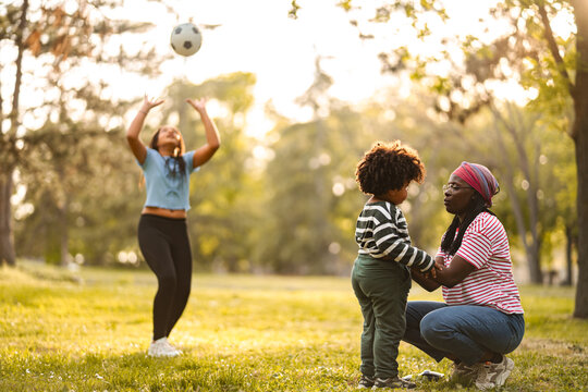 Mother and daugther playing football with child watching in park