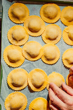 Hands arranging fresh homemade ravioli pasta on a tray
