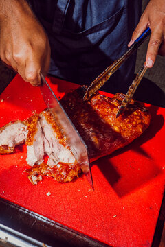 Chef slicing crispy roasted pork belly on a red cutting board.