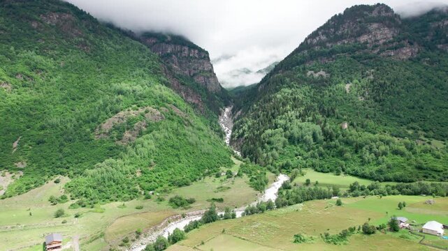 Cinematic drone flight above Zhabeshi village in Svaneti, Georgia. Stunning aerial view of green mountain valley, alpine river, dramatic Caucasus peaks and clouds, for travel, documentary, meditation 