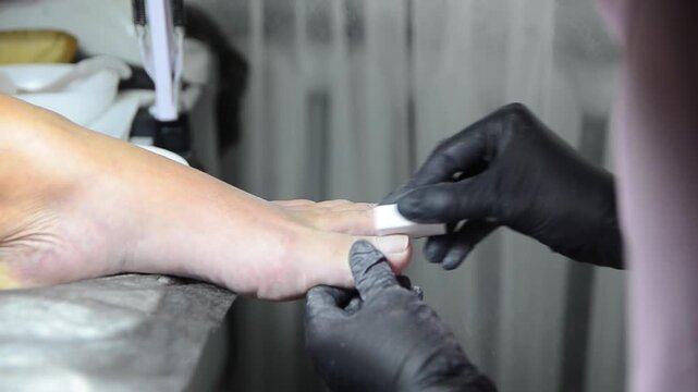 Professional pedicure master smoothing and buffing toenails with a nail buffer during a salon treatment. Close-up of foot care procedure preparing nails for the next stage of pedicure.
