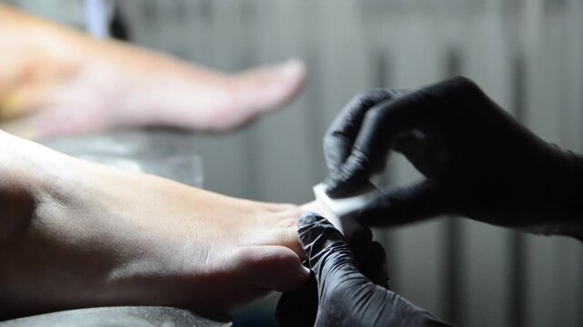 Professional pedicure master smoothing and buffing toenails with a nail buffer during a salon treatment. Close-up of foot care procedure preparing nails for the next stage of pedicure.