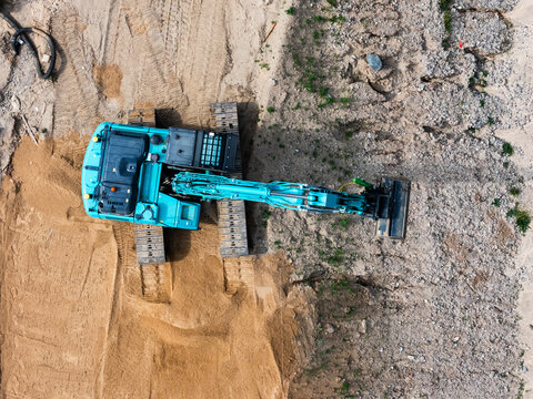 Aerial view of a teal excavator parked on a construction site with sandy soil and gravel in Kaunas, Kaunas County, Lithuania.