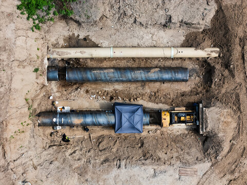 Aerial view of large industrial pipes being installed in a deep trench at a construction site in Kaunas, Kaunas County, Lithuania.