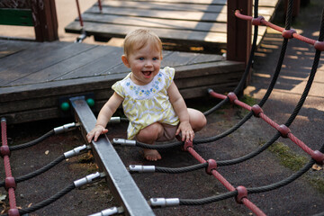 Fototapeta premium Toddler sitting on rope bridge element on outdoor playground in park