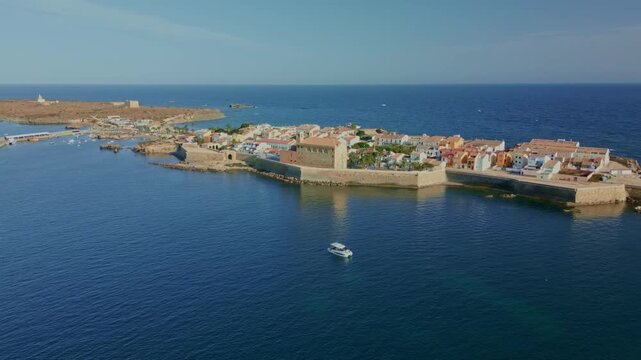 Tabarca island coastline in Spain, a small boat navigating the calm mediterranean sea with historic buildings and charming village architecture visible from an aerial perspective - stock video