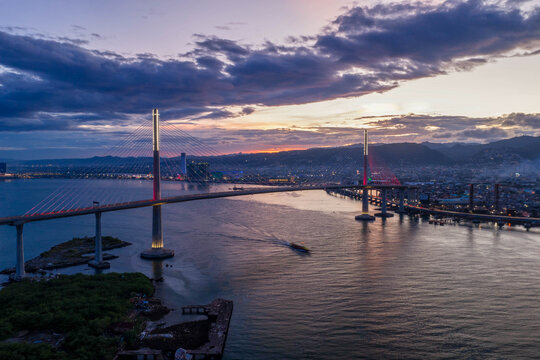 Aerial view of the Cebu-Cordova Link Expressway bridge illuminated at sunset with the city skyline in the background in Cebu City, Central Visayas, Philippines.