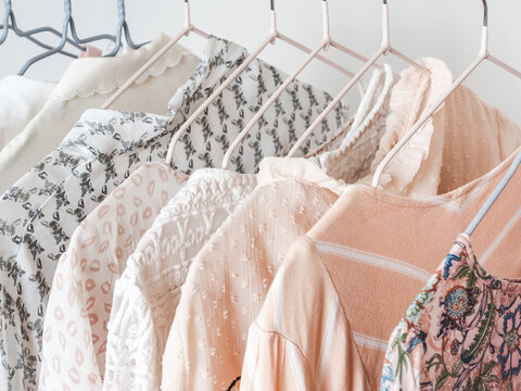 Feminine clothing rack with pastel blouses and dresses in cream, peach, and pink tones. Various patterns and textures on hangers. Symbolizes fashion, and style. Ideal for retail and lifestyle content