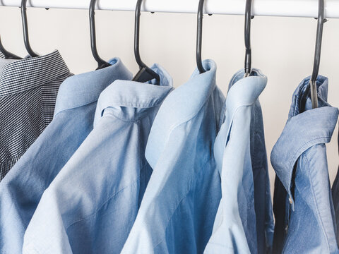 Men's blue shirts in various shades hanging on black hangers on a white clothing rack. Business and casual styles. Symbolizes professional wardrobe and fashion. Ideal for retail and lifestyle content
