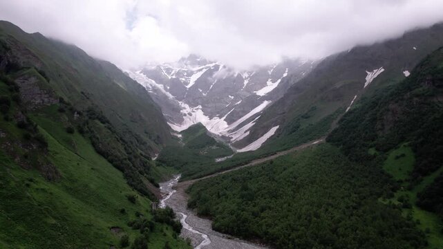 Epic cinematic drone flight above majestic green mountain valley with glaciers, winding serpentine road and lush Caucasus peaks in Svaneti, Georgia. for travel, meditation, wellness and nature project